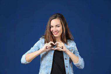 Renk arka plan üzerinde parmaklarını ile kalp yapma güzel gülümseyen kadın portresi
