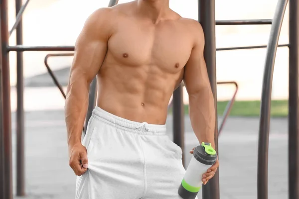 Handsome young man with protein drink in shaker outdoors