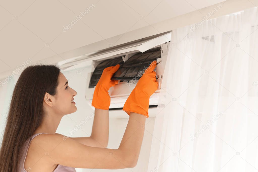 Young woman cleaning conditioner from dust indoors
