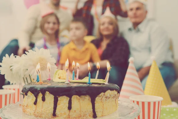 Birthday cake with alight candles and big family on background