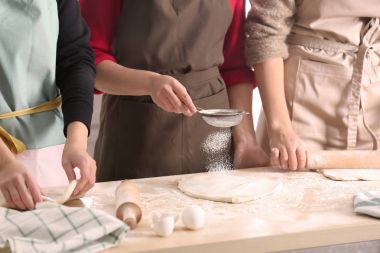 Young women preparing dough for pastries on kitchen table clipart