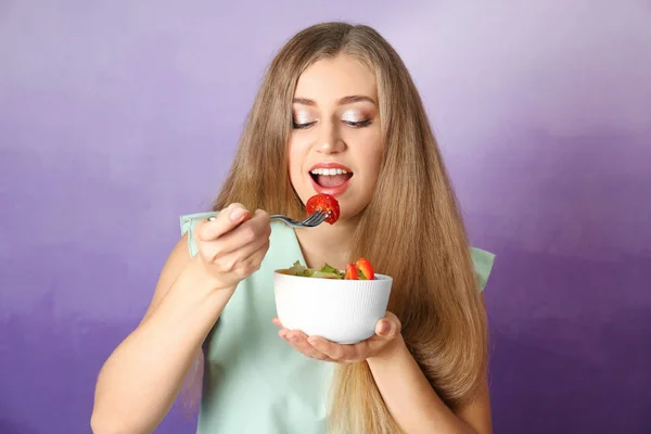 Joven hermosa mujer comiendo ensalada fresca sobre fondo de color — Foto de Stock