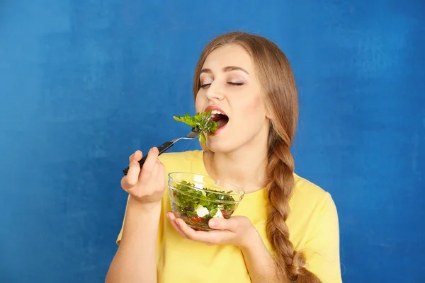 Joven hermosa mujer comiendo ensalada fresca sobre fondo de color — Foto de Stock