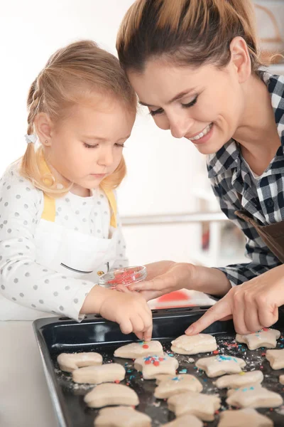 Mother and daughter decorating cookie dough with sprinkles indoors