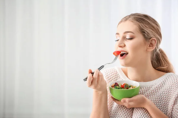 Jovem mulher bonita comendo salada fresca no fundo claro — Fotografia de Stock