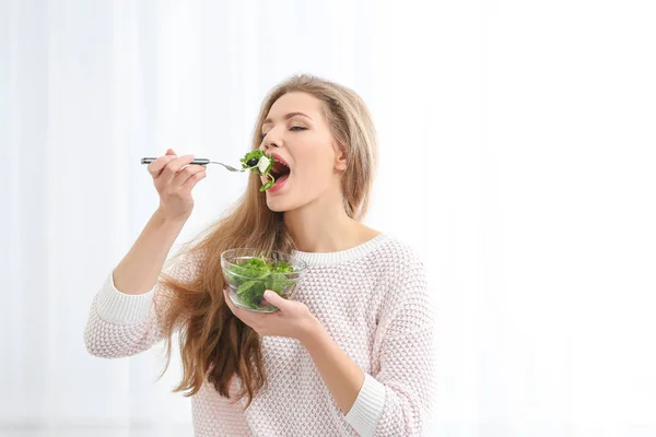 Giovane bella donna mangiare insalata fresca su sfondo chiaro — Foto Stock