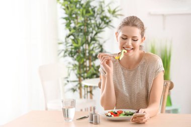 Genç ve güzel bir kadın evde taze salata yiyor.