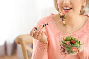 Genç ve güzel bir kadın evde taze salata yiyor.
