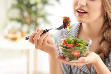Genç ve güzel bir kadın evde taze salata yiyor.