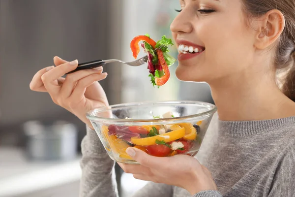 Joven hermosa mujer comiendo ensalada fresca sobre fondo borroso —  Fotos de Stock