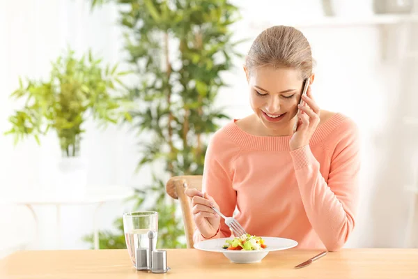 Młoda kobieta piękne rozmowy na telefon podczas jedzenia świeże sałatki w domu — Zdjęcie stockowe