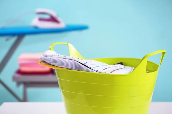 Plastic laundry basket with clothes on blurred background