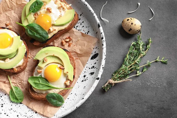 Tasty bruschettas with fried eggs and avocado on plate, closeup