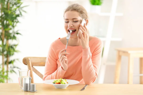 年轻美丽的妇女在电话边吃新鲜的沙拉在家里 — 图库照片