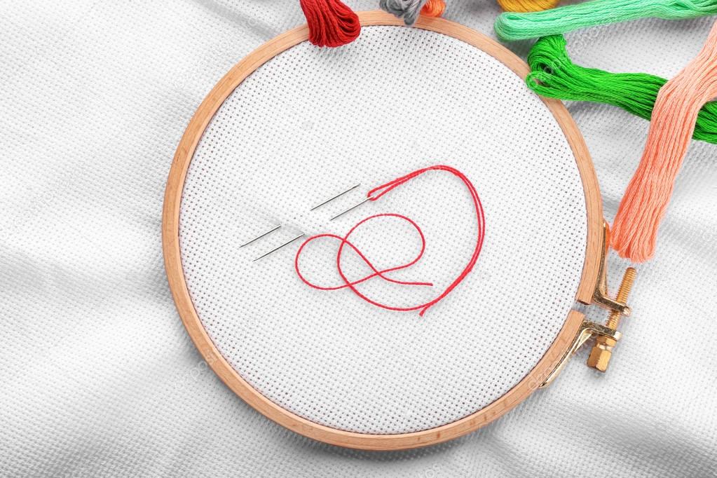 Embroidery hoop with fabric, sewing needles and thread, top view
