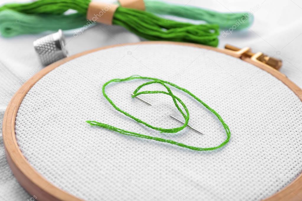 Embroidery hoop with fabric, sewing needle and thread, closeup