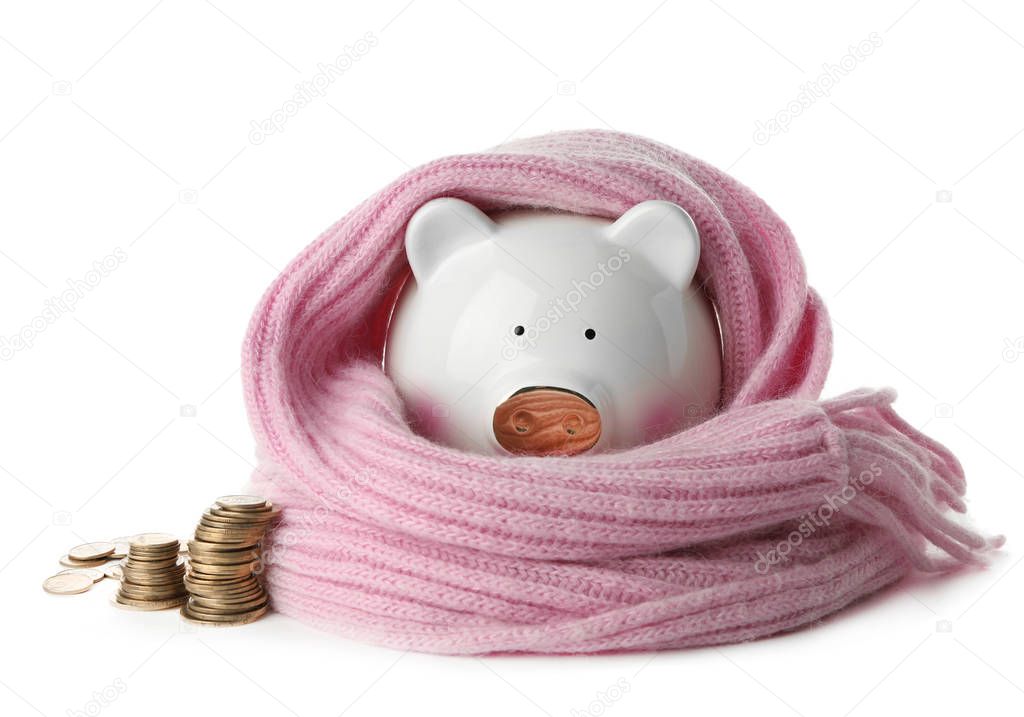 Piggy bank with warm scarf and coins on white background