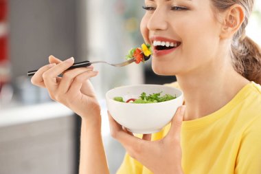 Genç ve güzel bir kadın evde taze salata yiyor.