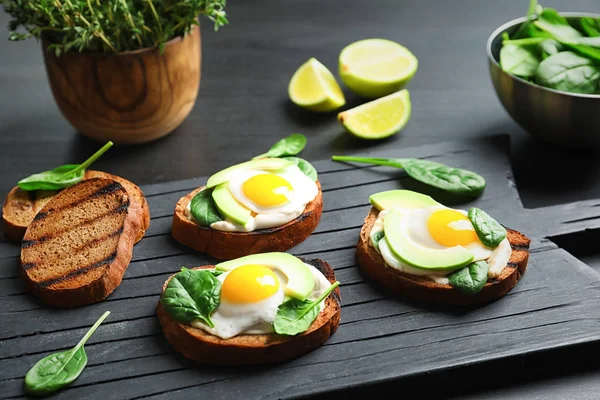 Tasty bruschettas with fried eggs and avocado on wooden board