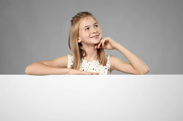 Sød pige med blank reklame bord på grå baggrund - Stock-foto