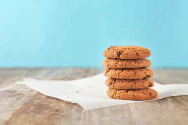 Ahşap masa mavi duvarın üzerinde çikolata parçaları ile lezzetli yulaf ezmeli kurabiye yığını