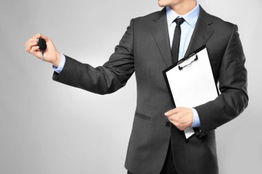 Yakışıklı araba satıcısı ile anahtar ve gri arka plan üzerinde Pano