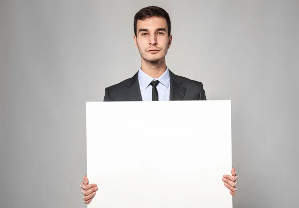 Красивый бизнесмен с пустой рекламной доской на сером фоне — стоковое фото