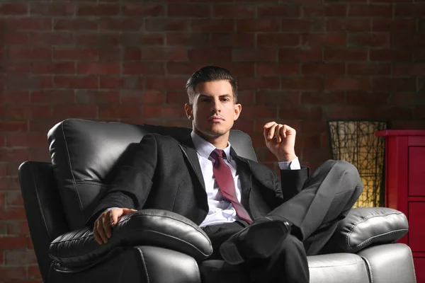 Hombre joven guapo en traje elegante sentado en sillón en el interior —  Fotos de Stock