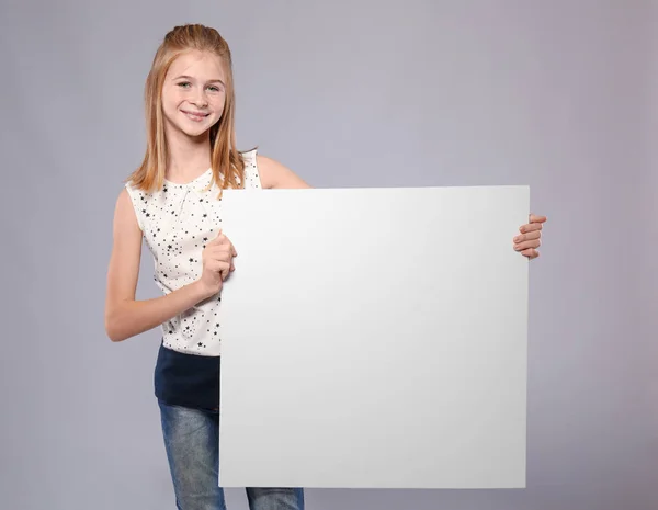 Menina bonito com placa de publicidade em branco no fundo cinza — Fotografia de Stock