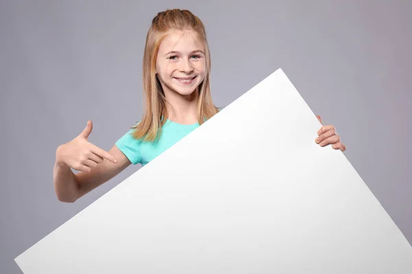 Menina bonito com placa de publicidade em branco no fundo cinza — Fotografia de Stock