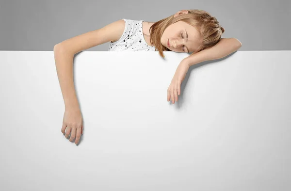 Linda chica dormida con tablero de publicidad en blanco sobre fondo gris — Foto de Stock