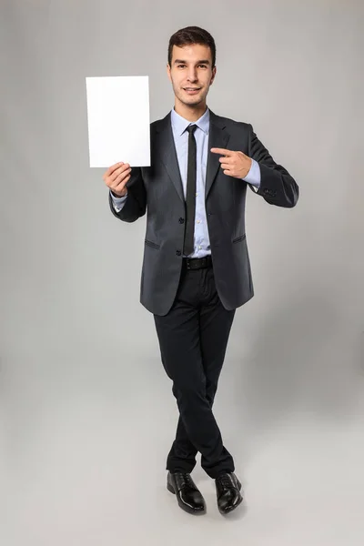 Stilig affärsman med tomt pappersark för reklam på grå bakgrund — Stockfoto