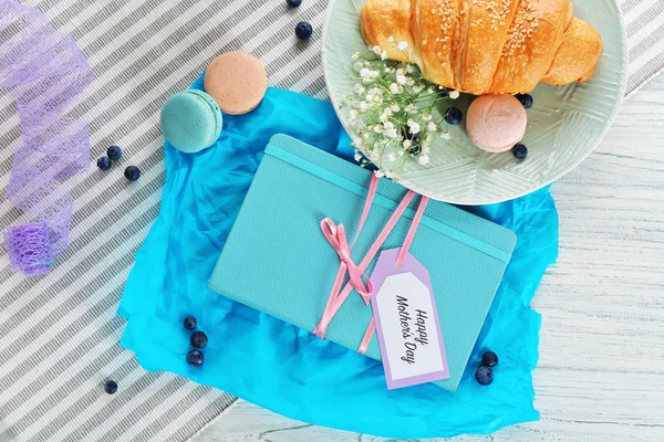 Kort med ord ”glad mors dag” notebook och välsmakande croissant på bordsskivan, Visa — Stockfoto