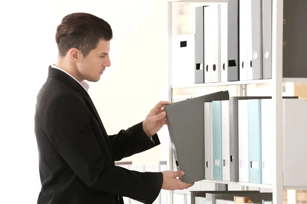 Young man taking folder with documents from shelf in archive