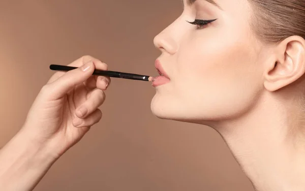 Artista profesional de visage aplicando maquillaje en la cara de la mujer sobre el fondo de color —  Fotos de Stock