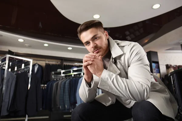 Молодой человек в стильном пальто в магазине мужской одежды — стоковое фото