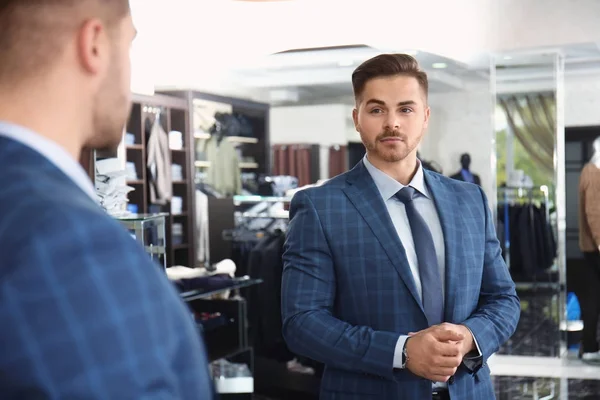 Guapo joven vestido de traje mirando en el espejo en la tienda — Foto de Stock