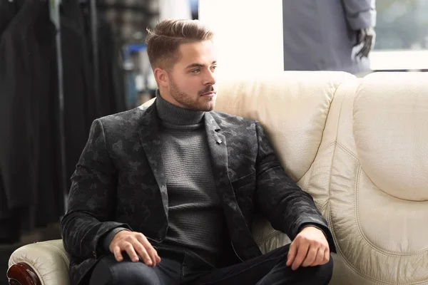 Az elegáns ruhákat, ül a kanapén férfi boltban fiatalember — Stock Fotó