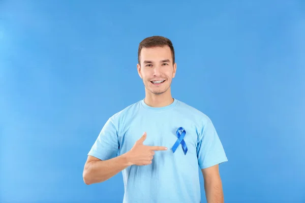 Joven apuntando a la cinta azul en su camiseta contra el fondo de color. Concepto de conciencia del cáncer de próstata — Foto de Stock