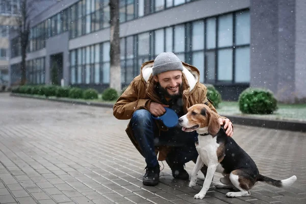 Bonito jovem hipster andando seu cão ao ar livre no dia nevado — Fotografia de Stock