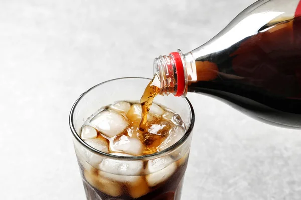 Versare la cola dalla bottiglia in vetro con ghiaccio su fondo chiaro, primo piano — Foto Stock