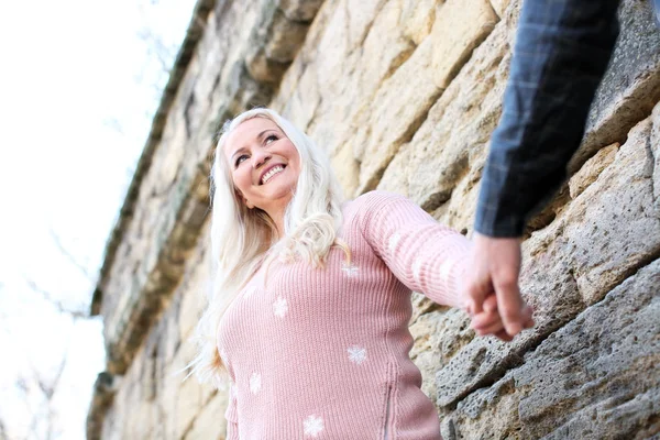 Mujer madura feliz sosteniendo la mano de su marido cerca de la pared de ladrillo al aire libre — Foto de Stock