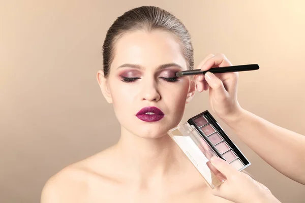 Профессиональный визажист наносит макияж на лицо женщины на цветном фоне — стоковое фото
