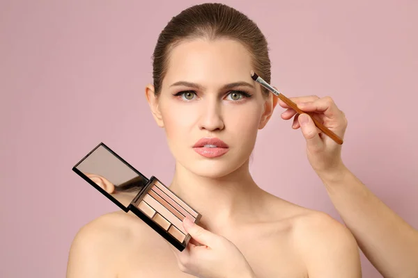 Artista de visage profesional aplicando maquillaje en la cara de la mujer sobre fondo claro — Foto de Stock