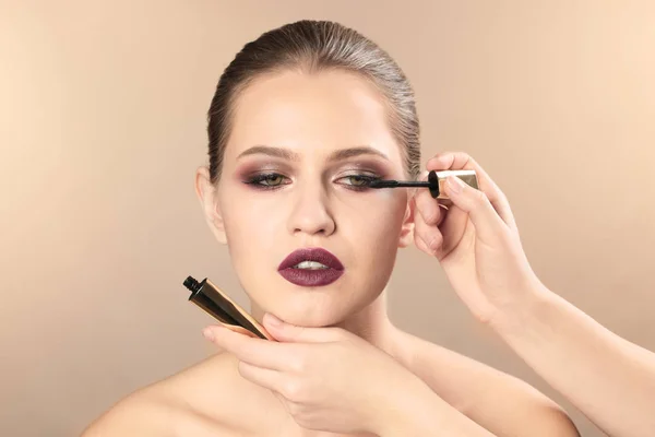 Professionele visage kunstenaar toepassing van make-up op vrouw gezicht op kleur achtergrond — Stockfoto