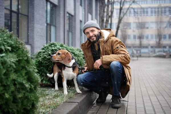 Guapo joven hipster paseando a su perro al aire libre en día nevado —  Fotos de Stock