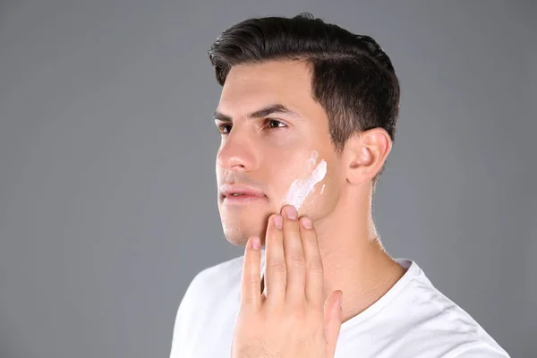 Hombre guapo aplicando crema facial sobre fondo gris — Foto de Stock