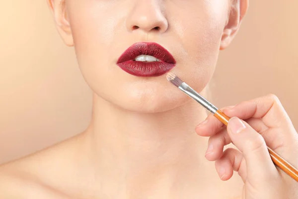 Professionele visage kunstenaar toepassing van make-up op vrouw gezicht op kleur achtergrond — Stockfoto