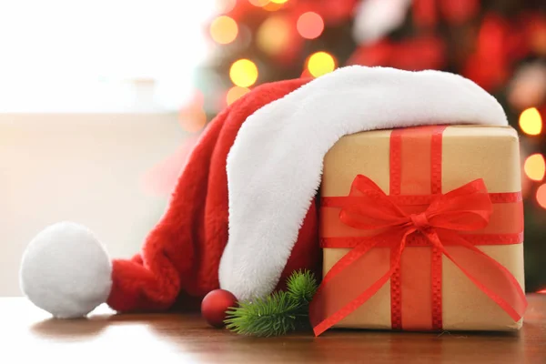 Wrapped gift and Christmas hat on table against blurred festive lights. Boxing day — Stock Photo, Image