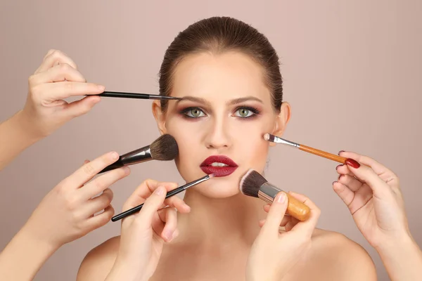 Artistas profesionales de visage aplicando maquillaje en la cara de la mujer sobre fondo claro — Foto de Stock